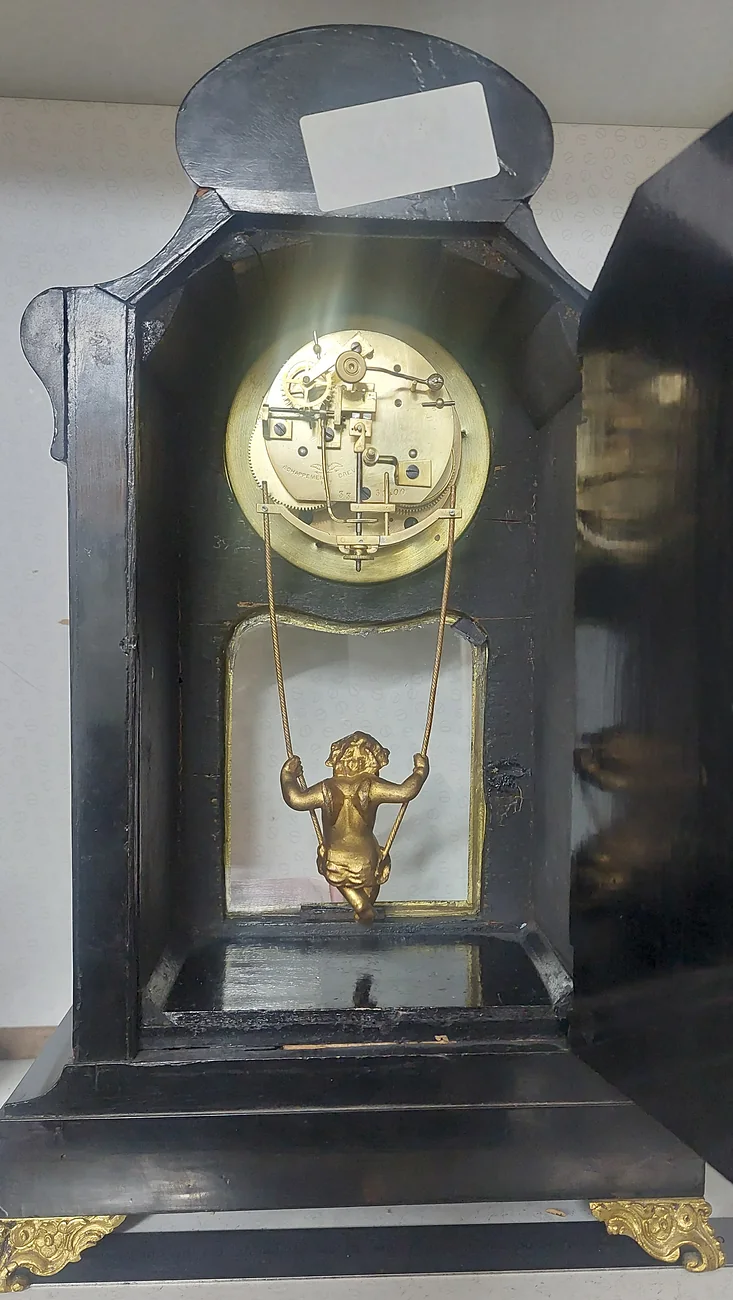A rare French clock seen from the back with its door open, showing the movement and a gilt figure on a swing beneath it
