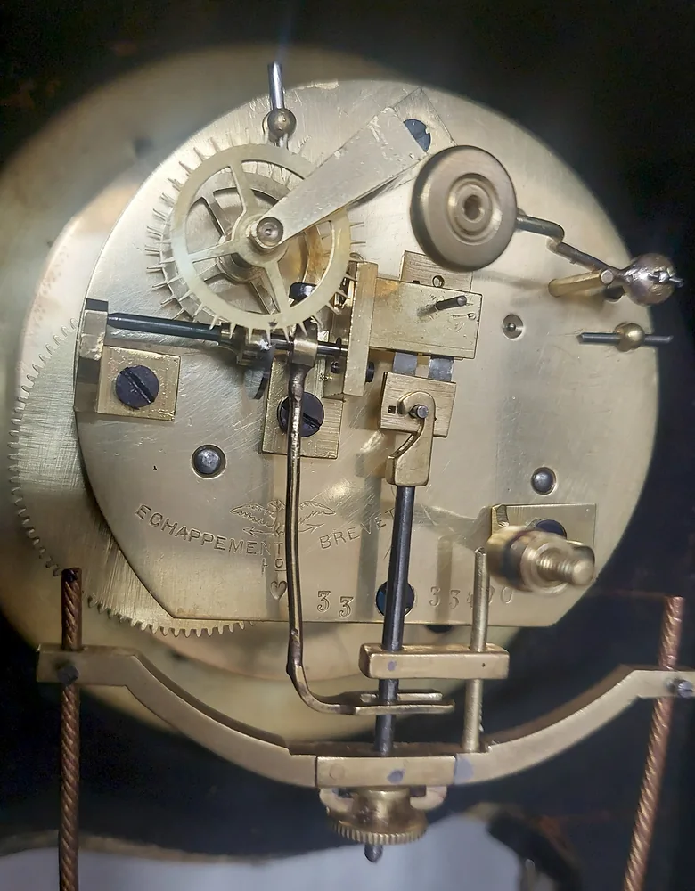 The back of a French clock movement stamped 'Échappement breveté', with the cords of a swing hanging below it
