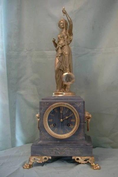 A Guilmet mystery clock: a gilt figure on a dark plinth holds the pendulum aloft, with the dial set in the plinth below