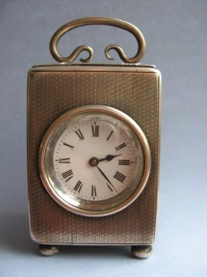 A small silver-cased carriage clock with an engine-turned case and a loop handle